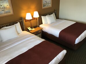 A hotel room with two beds, each with white linens and a brown throw blanket. There is a nightstand with a lamp and a telephone between the beds. - AmericInn by Wyndham Cody (Cody)