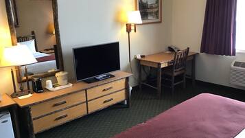 A hotel room with a bed, a desk with a chair, a television, a dresser, a lamp, and a painting on the wall.