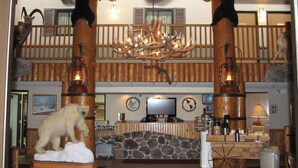 A rustic lodge interior with a stone fireplace, wooden beams, and antler chandeliers. - AmericInn by Wyndham Cody (Cody)