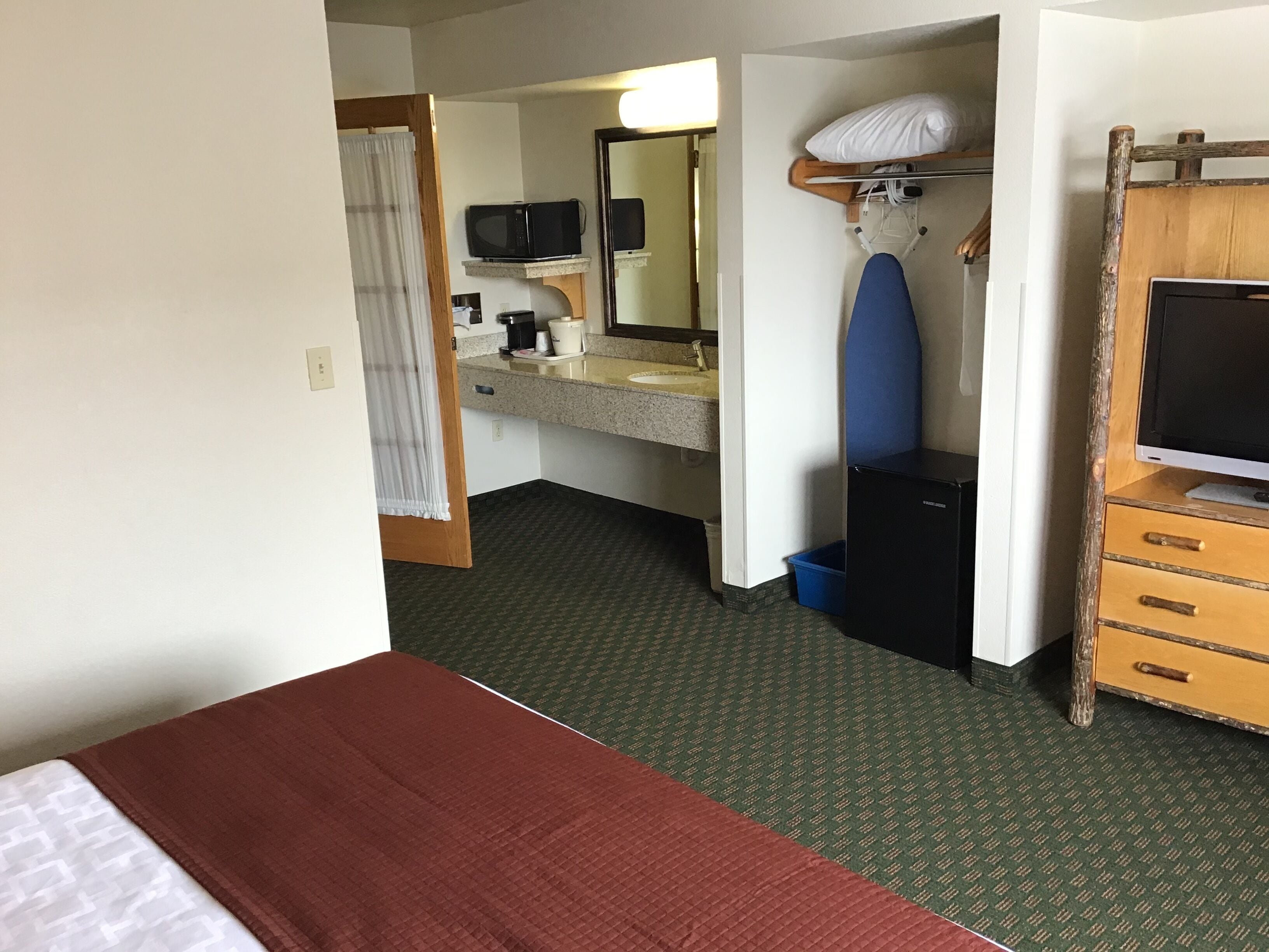 A hotel room with a bed, a desk, a television, a microwave, a sink, and a mirror.