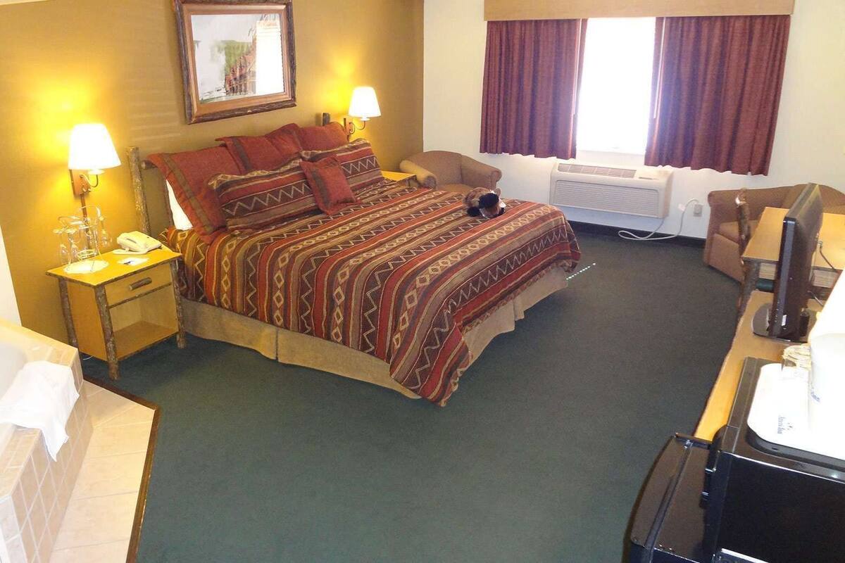 A hotel room with a bed, a desk, a chair, a desk lamp, a telephone, and a window with curtains.
