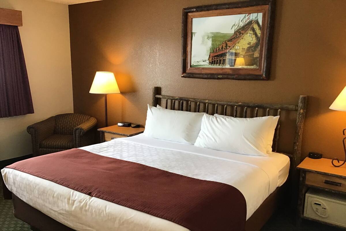 A hotel room with a large bed, two bedside tables, a chair, a lamp, and a framed picture on the wall.