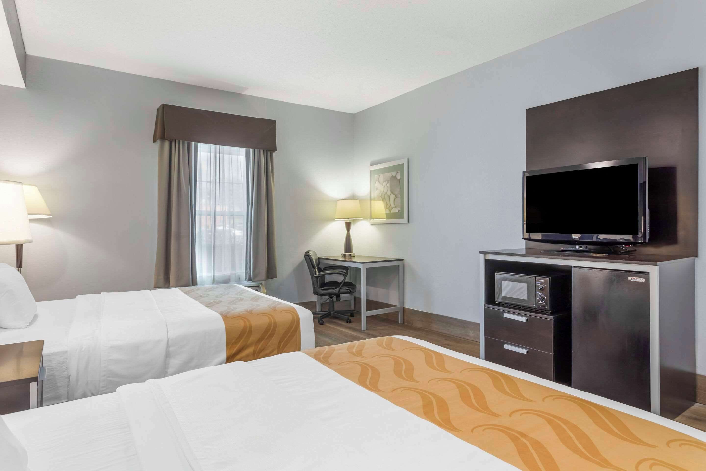 A hotel room with two beds, a desk with a chair, a television, and a microwave.