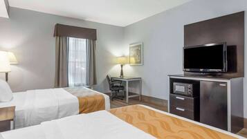 A hotel room with two beds, a desk with a chair, a television, and a microwave.