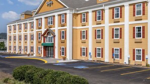 Ein mehrstöckiges Hotel mit gelber Fassade, roten Fensterläden und einem grünen Markisenvorzelt.
