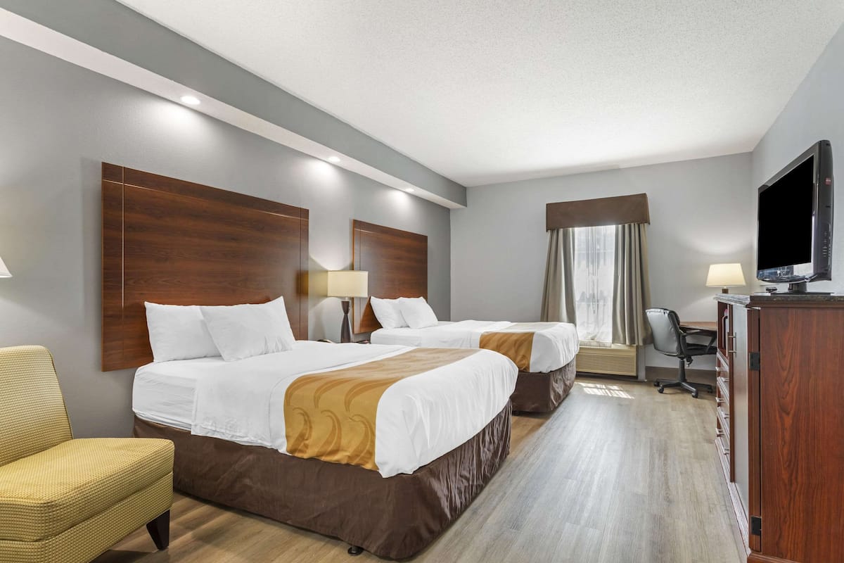 A hotel room with two beds, a desk, a television, and a chair.