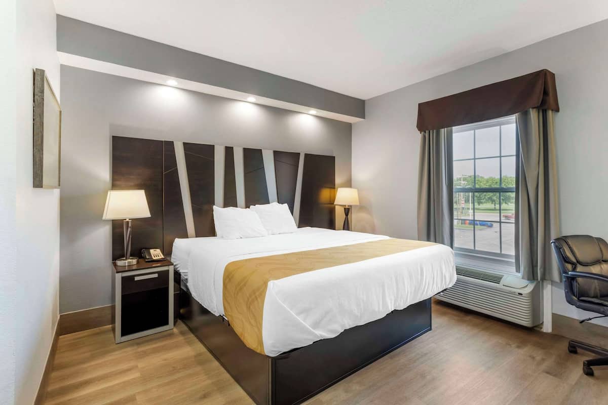 A hotel room with a large bed, bedside lamps, a small table with a phone, a chair, and a window with curtains.