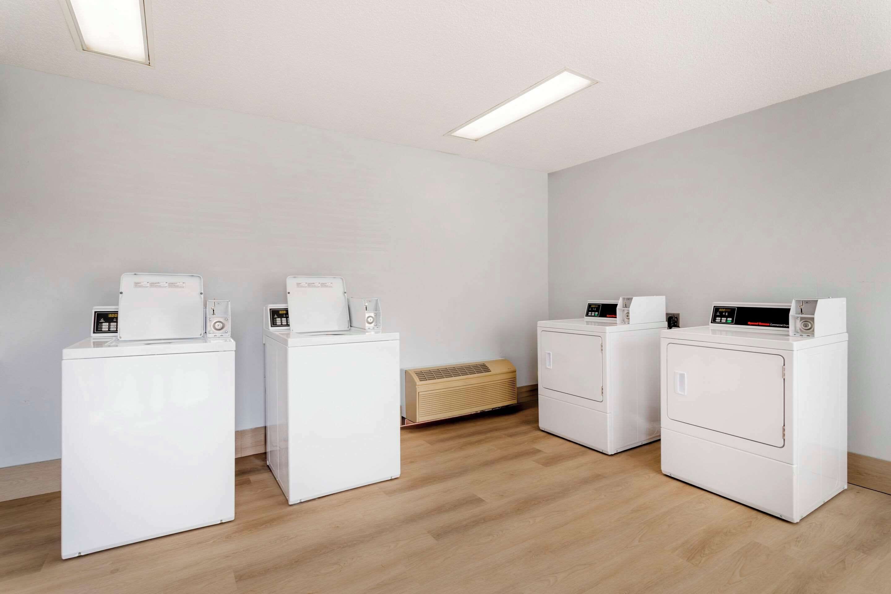 A laundry room with four white washing machines, a wooden floor, and a ceiling light.
