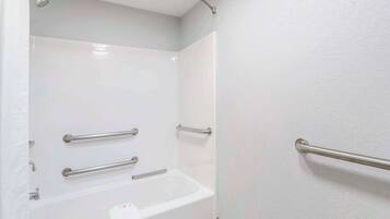 A bathroom with a white bathtub, grab bars, and a towel rack.