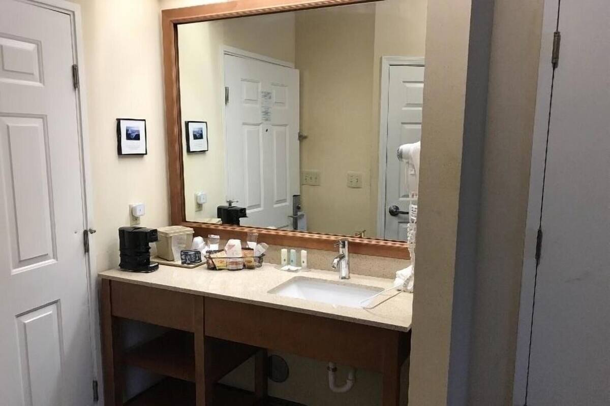 A hotel bathroom with a double sink, a large mirror, and a coffee maker.