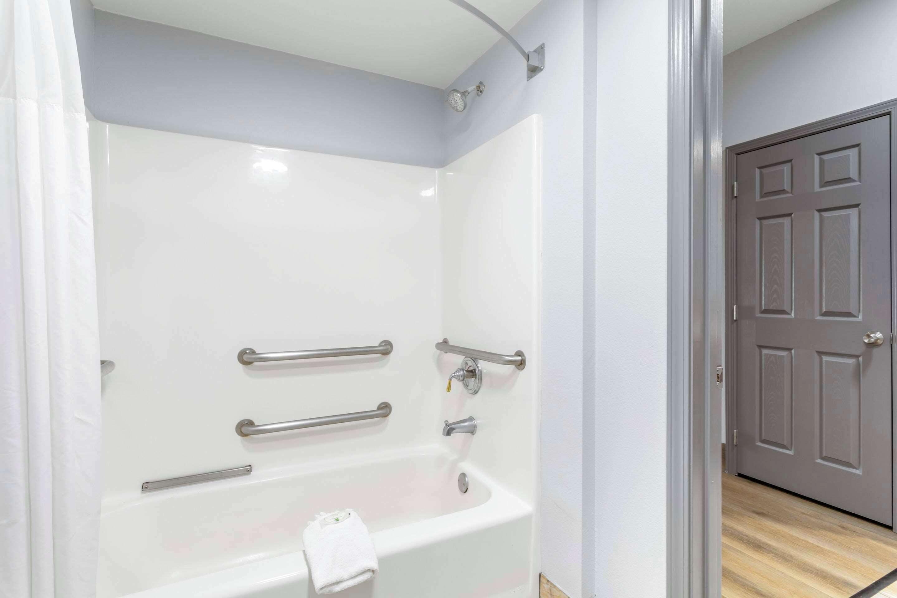 A bathroom with a white bathtub, grab bars, and a towel rack.
