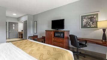 A hotel room with a bed, a desk with a chair, a television, a microwave, and a framed picture on the wall.