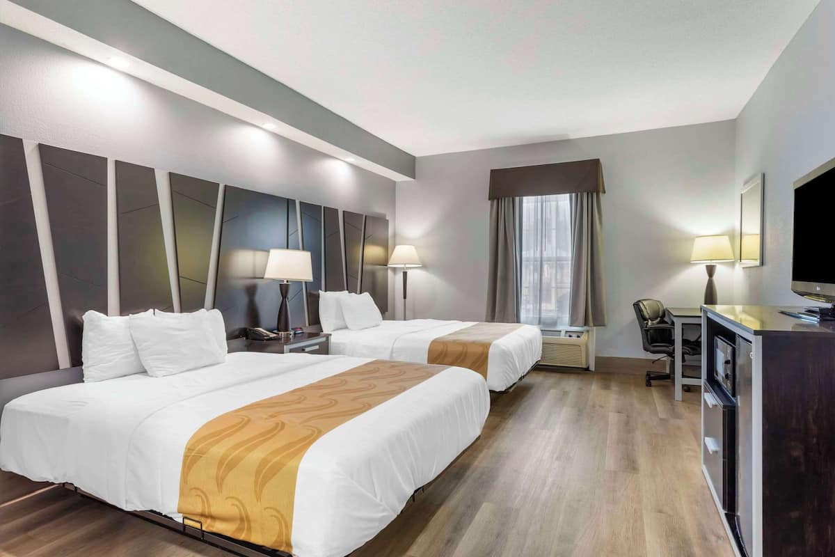 A hotel room with two beds, a desk with a chair, a TV, and a minibar.