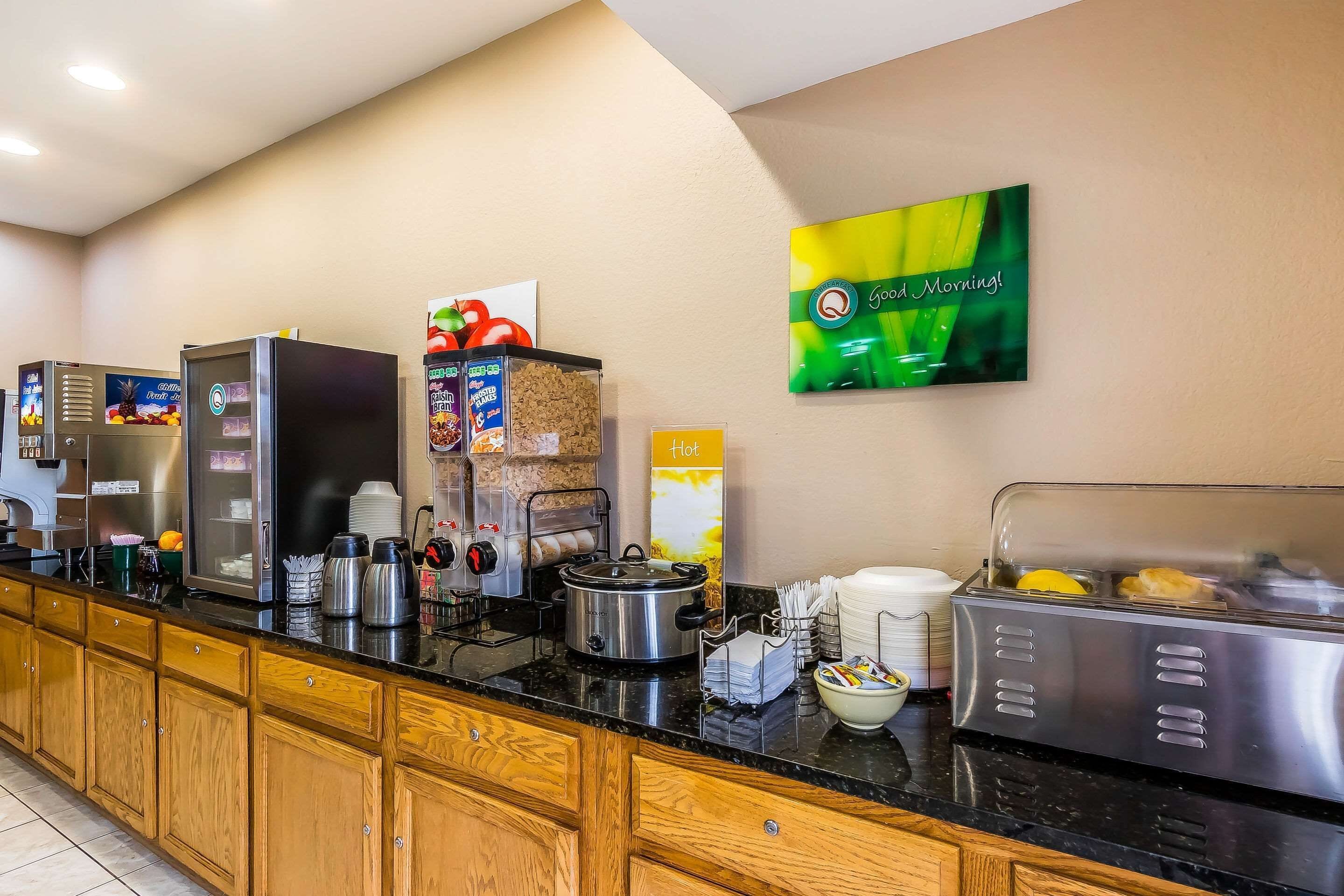 Un área de desayuno de hotel con máquinas de café de servicio libre, un dispensador de fruta, un dispensador de cereales y una tostadora.