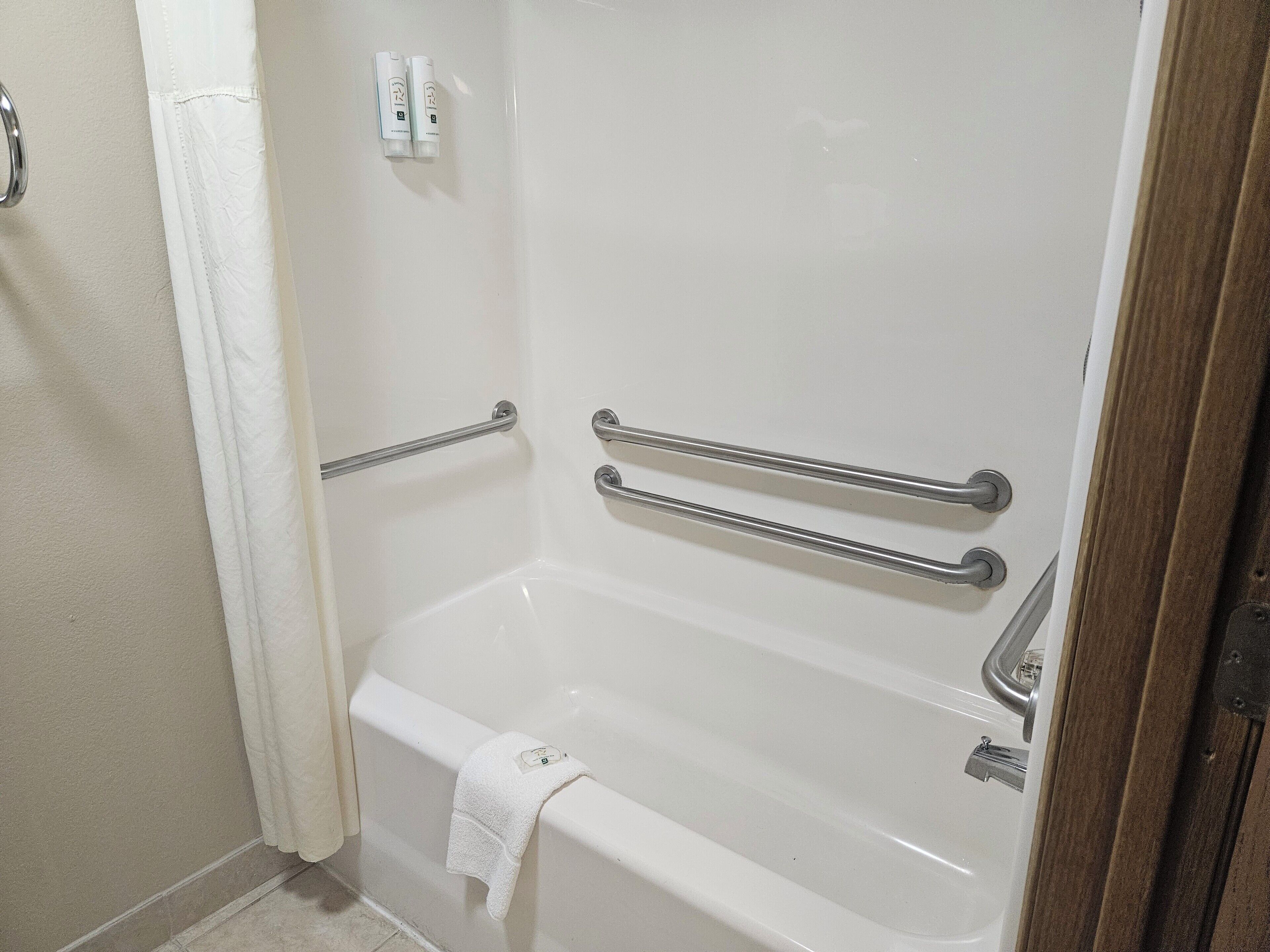A white bathtub with grab bars and a towel rack.