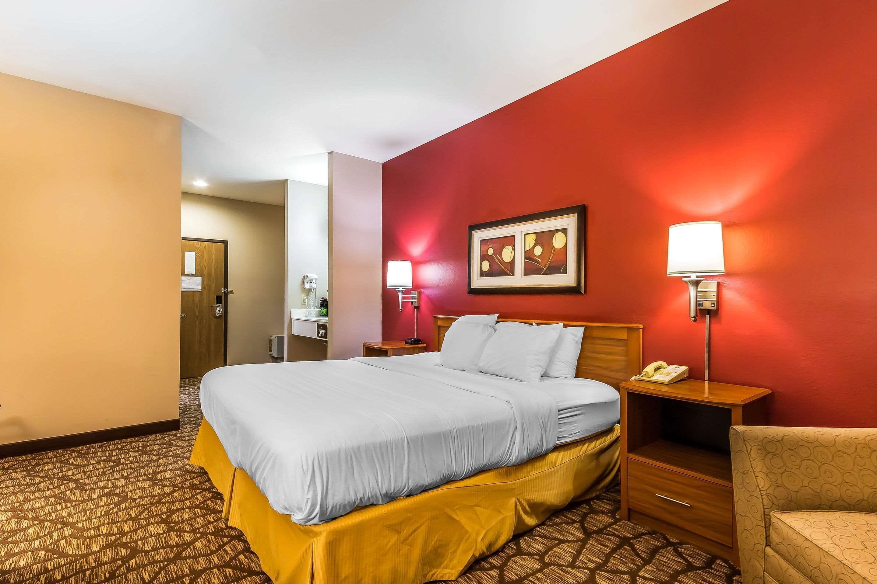 A hotel room with a large bed, a bedside table with a lamp, a chair, and a desk with a telephone.