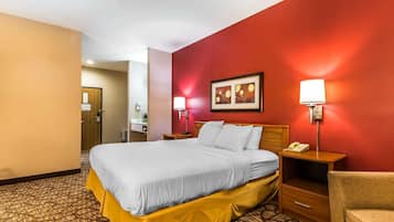 A hotel room with a large bed, a bedside table with a lamp, a chair, and a desk with a telephone.