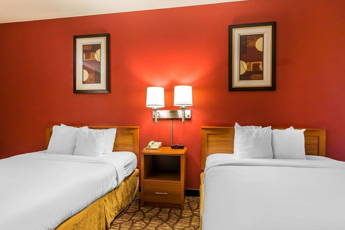 A hotel room with two beds, a nightstand with a lamp, and two framed pictures on the wall.