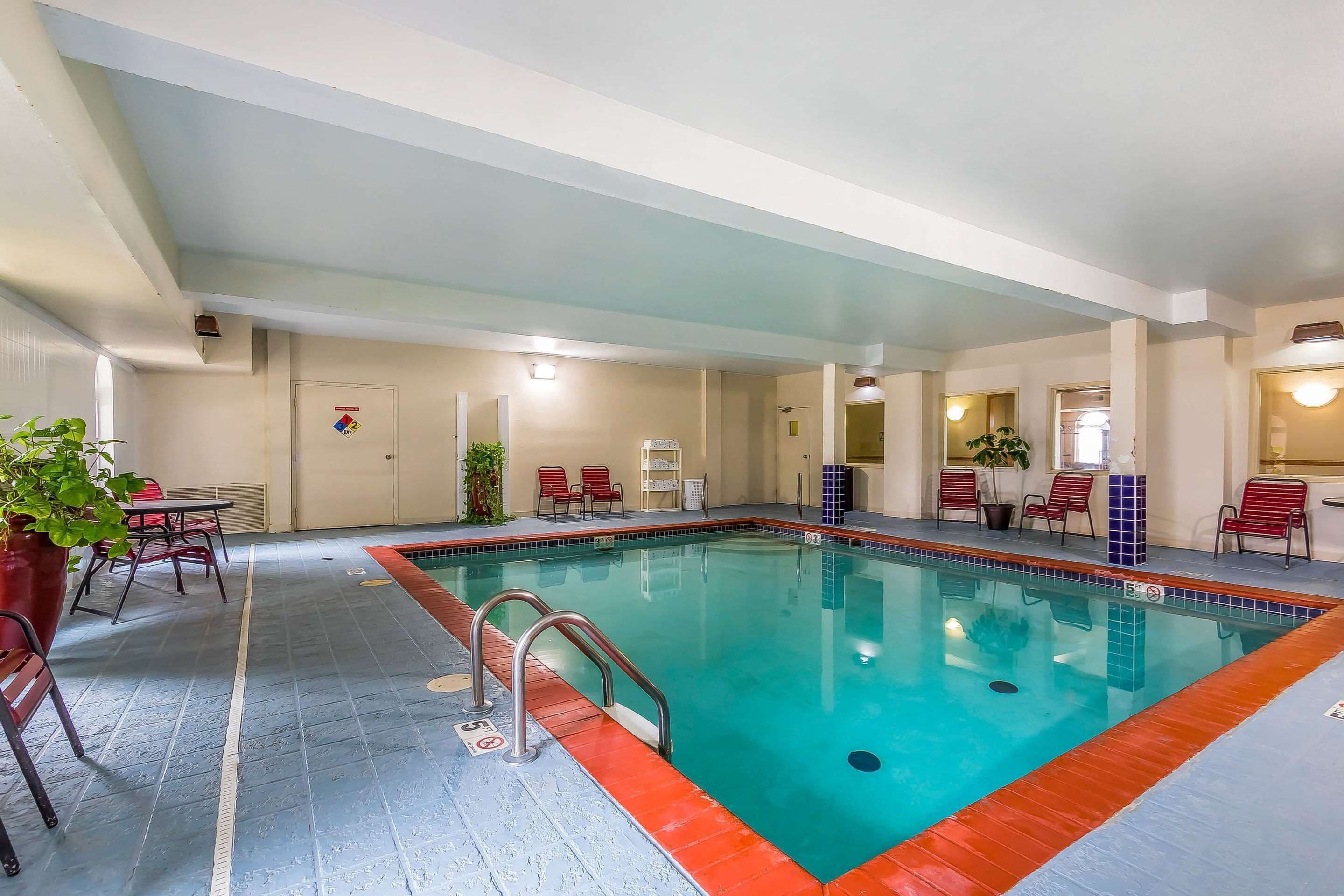 Una piscina interna con bordo rosso, circondata da sedie rosse e un tavolo.