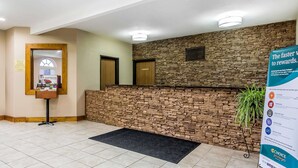 Un área de recepción con pared de piedra, un mostrador de recepción, una planta y un cartel.