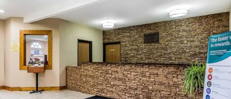 Un área de recepción con pared de piedra, un mostrador de recepción, una planta y un cartel.