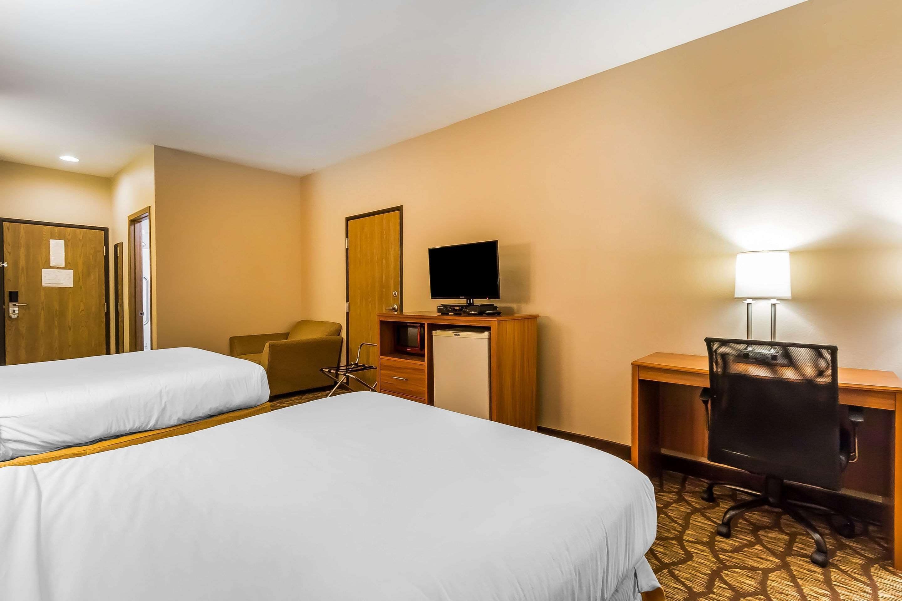 Une chambre d’hôtel avec deux lits, un bureau avec un ordinateur, une chaise, une télévision et une lampe de bureau.