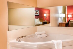 A hotel bathroom with a large bathtub, a mirror, and a red wall.