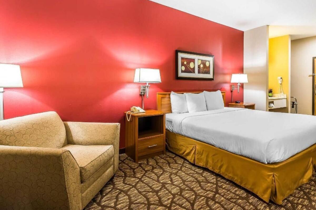 A hotel room with a bed, two bedside tables, a chair, and a red accent wall.