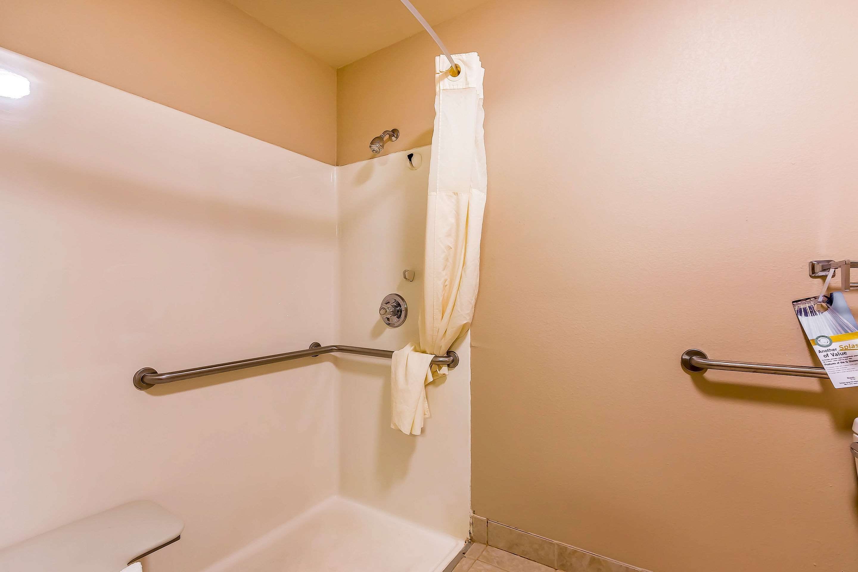 A shower area with a white shower curtain, grab bars, and a white bathtub.
