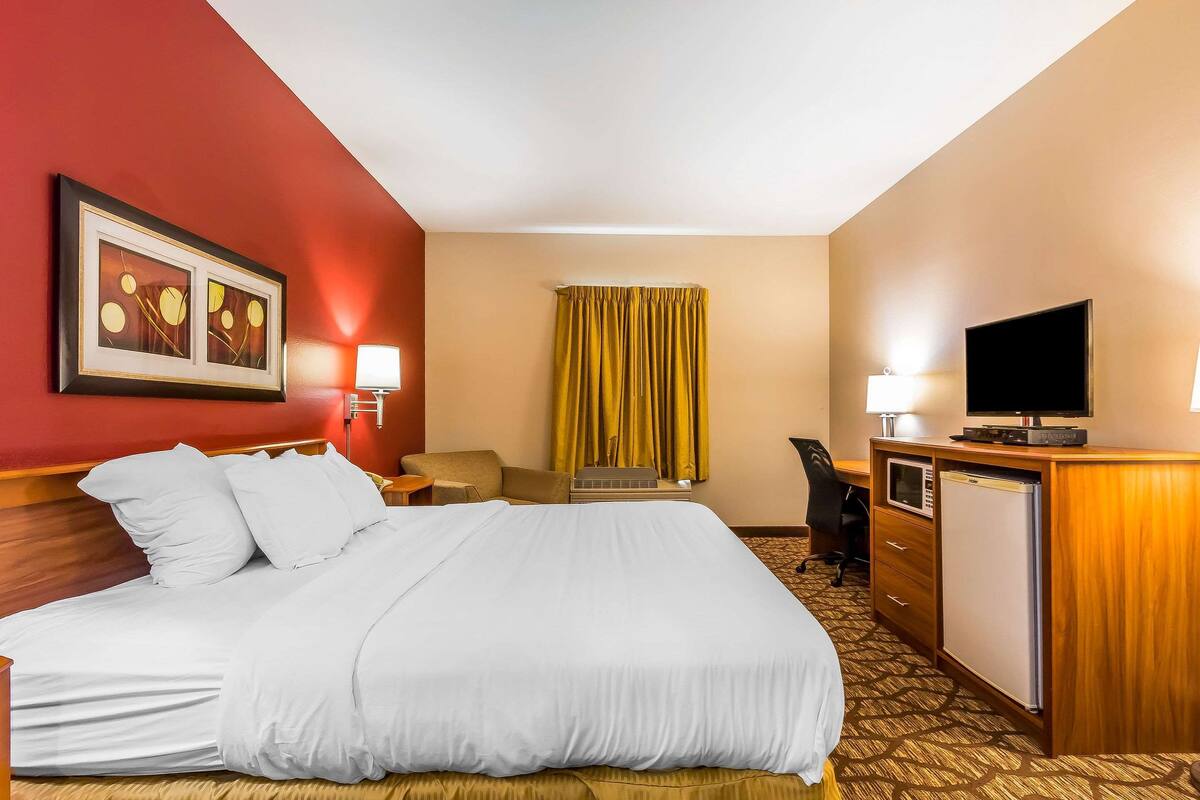 A hotel room with a large bed, a desk with a computer, a television, and a minibar.