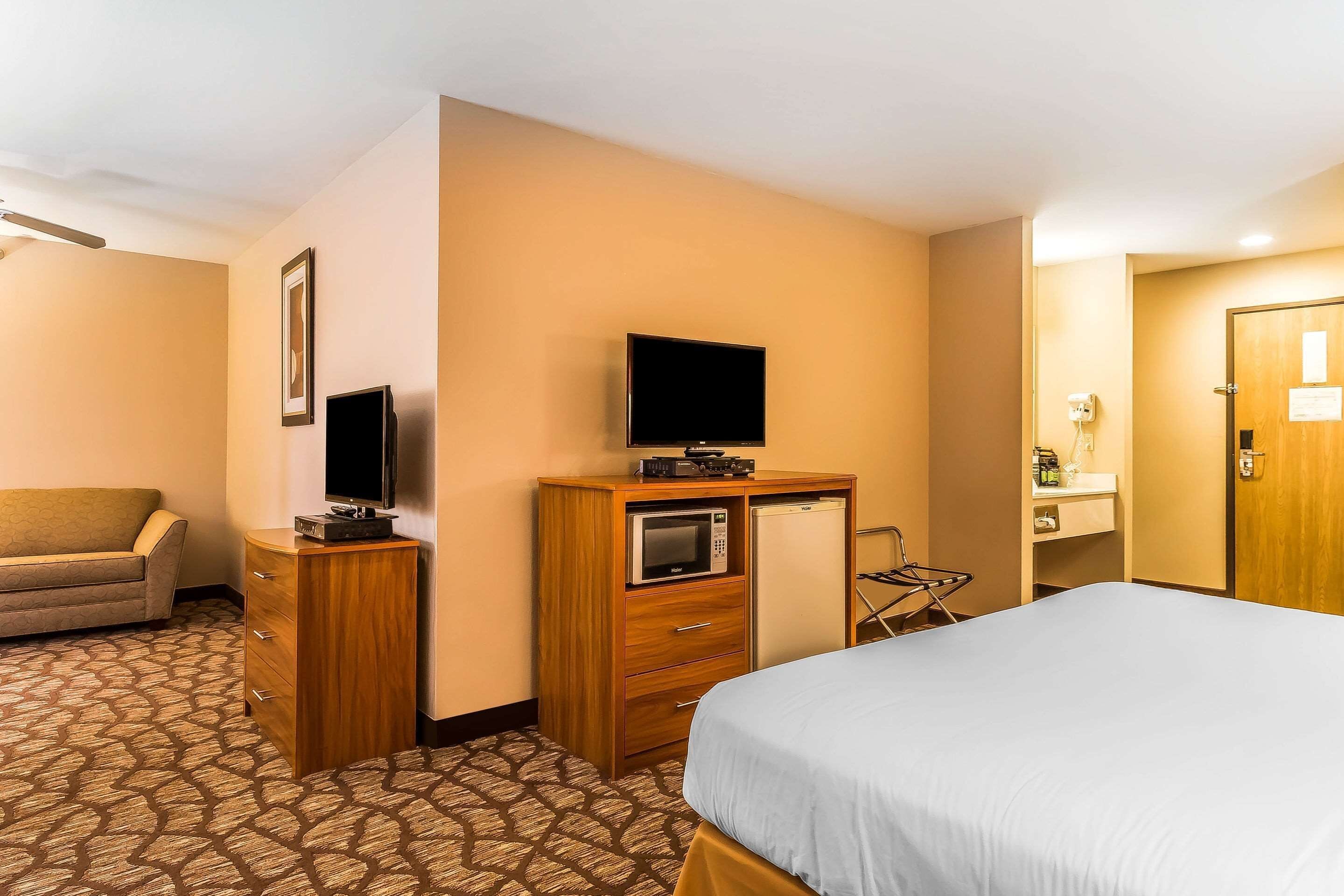 Une chambre d’hôtel comprenant un lit, une commode en bois avec un téléviseur, un four à micro-ondes et un petit réfrigérateur.