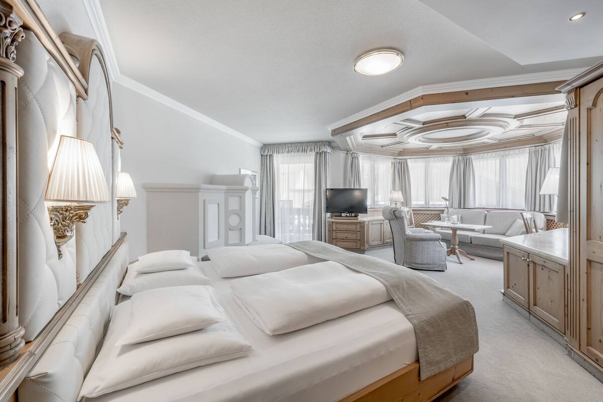 A hotel room with a large bed, a desk, a television, and a seating area with a view of the city.