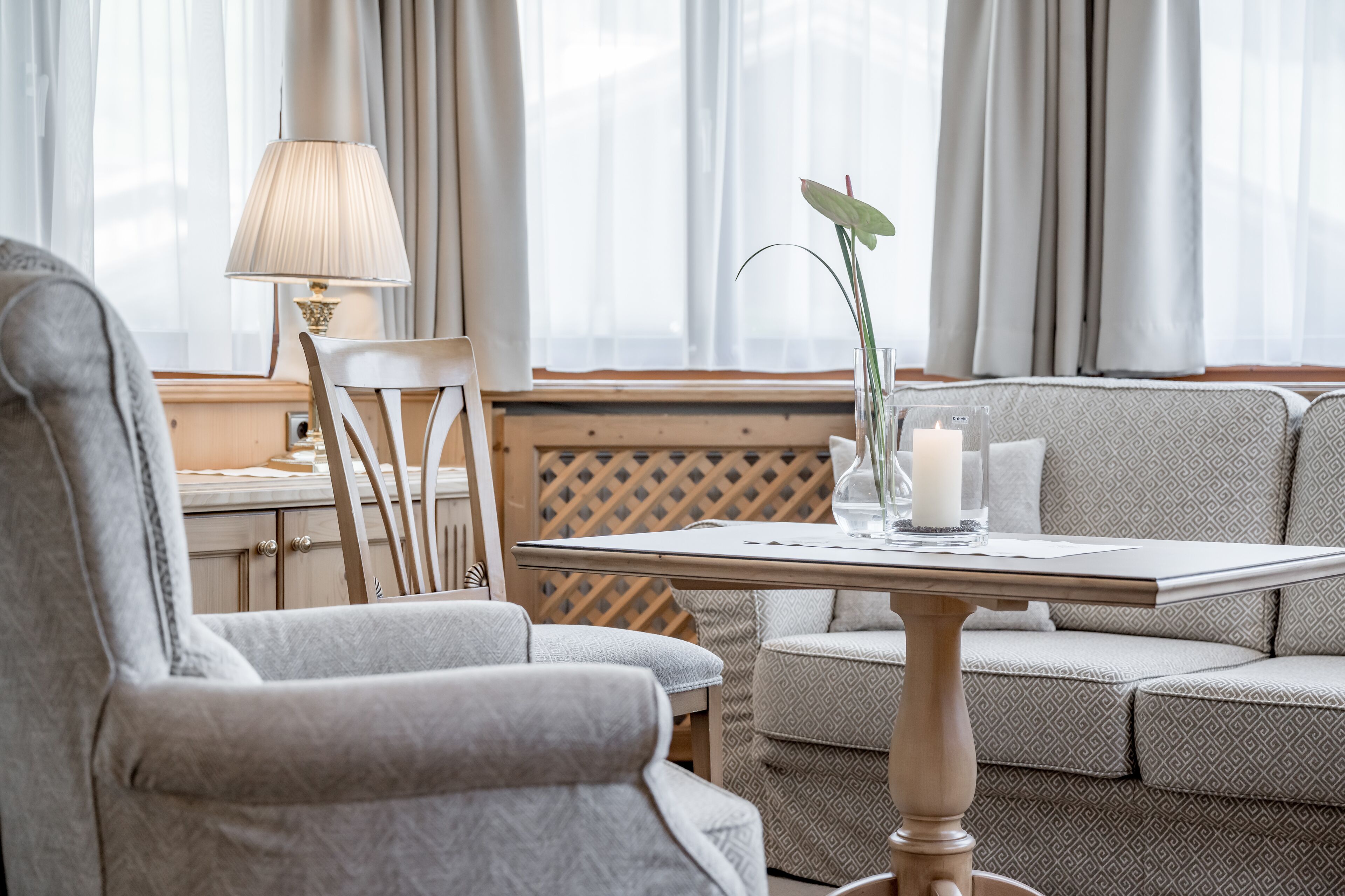 A hotel room with a sofa, armchair, and a small table with a lamp and a vase with a plant.
