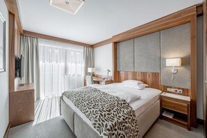 A modern hotel room with a large bed, a wooden headboard, a desk with a lamp, and a TV on a wooden stand.