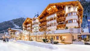 Un hotel de varios pisos con balcones, un paisaje nevado y montañas al fondo.