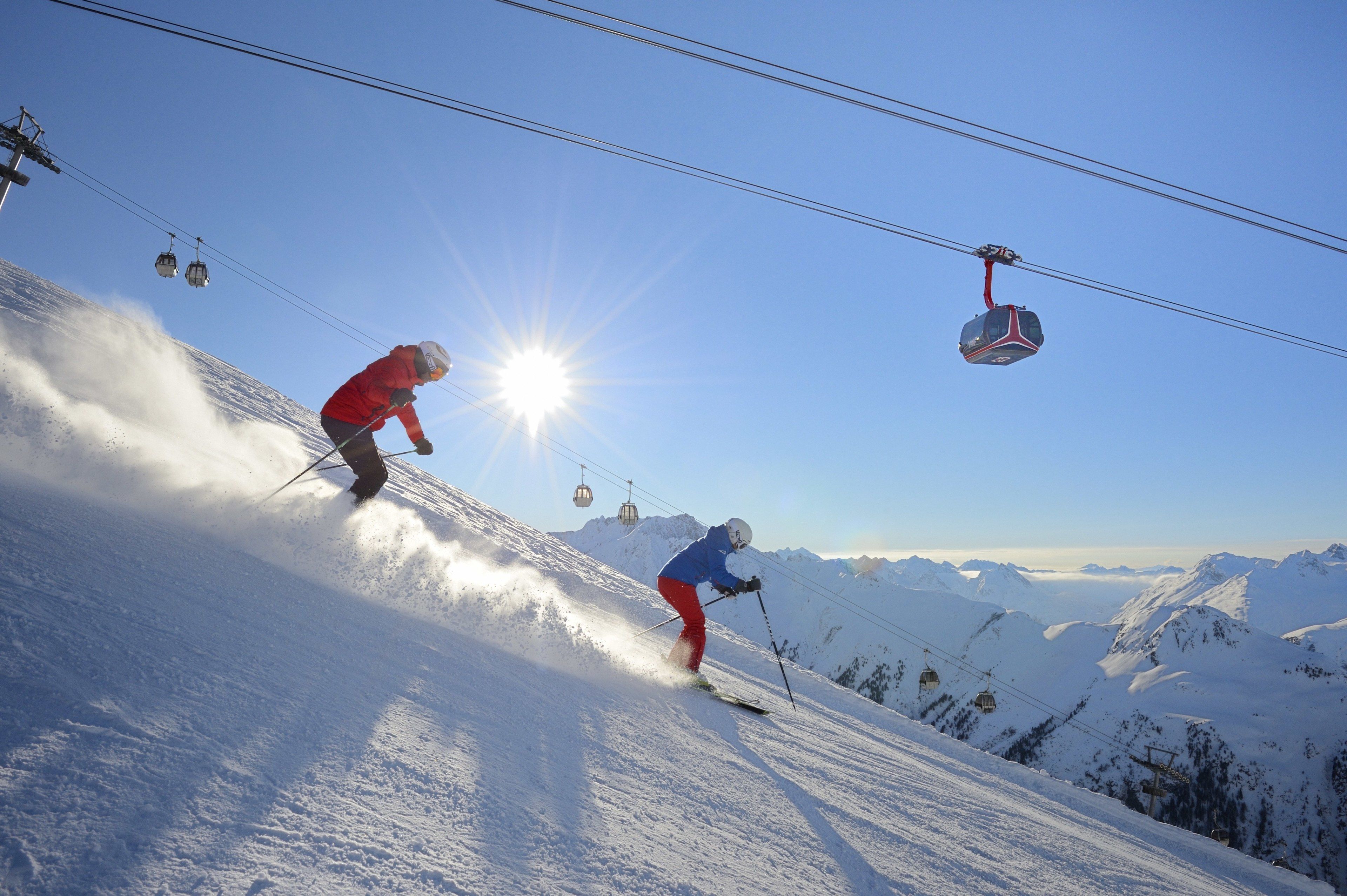Een skipiste met skiërs en een kabelbaan op de achtergrond.