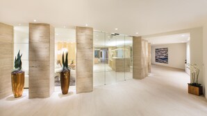 Un moderno vestíbulo de hotel con un diseño minimalista, que presenta un separador de vidrio, columnas de madera y plantas en macetas.