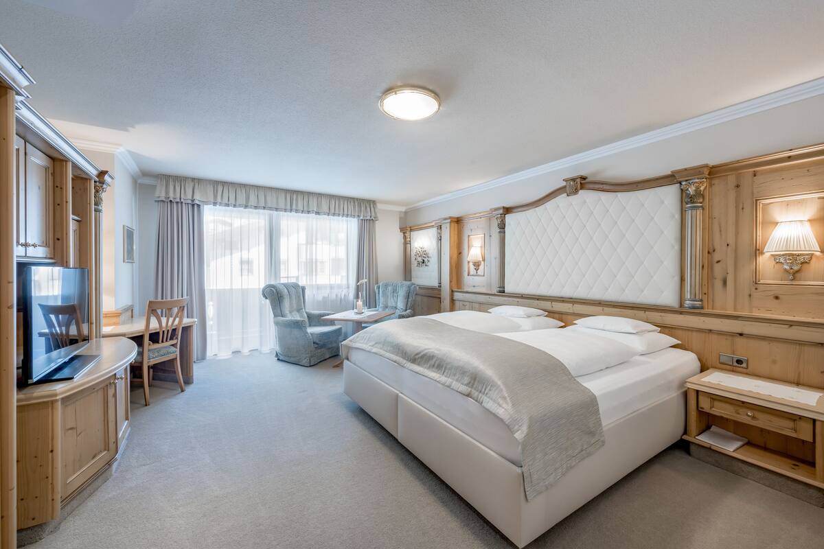 A hotel room with a large bed, a desk with a chair, a television, and a lamp.