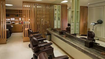A hair salon with multiple leather chairs, a reception desk, and a mirror reflecting the interior.