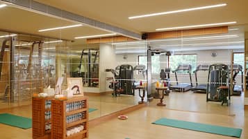Un gimnasio con equipo de ejercicio, un estante para botellas de agua y colchonetas verdes en el suelo.