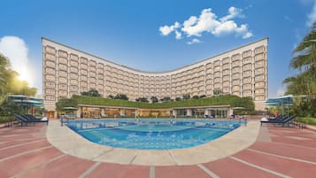 Experience the hotel's striking facade and unwind by the pool surrounded by lush greenery and comfortable lounge chairs.