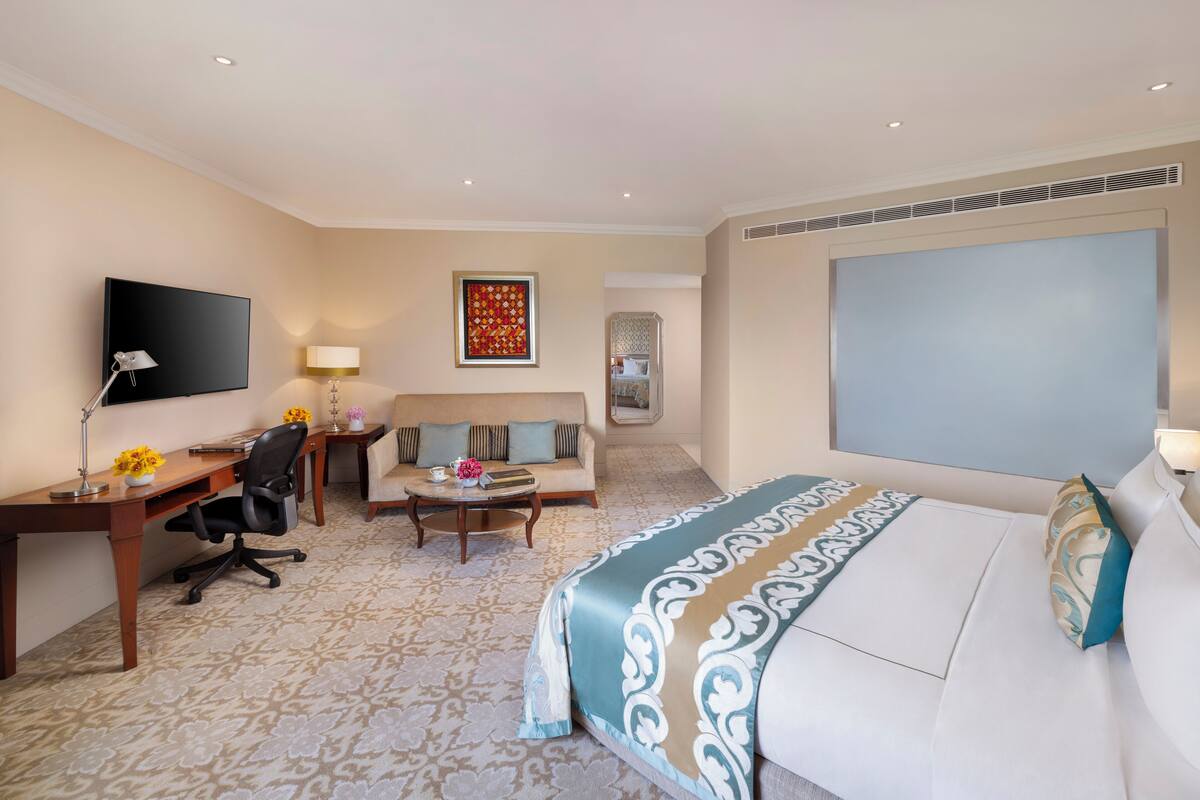 A hotel room with a bed, a desk, a chair, a sofa, a TV, and a decorative wall piece.