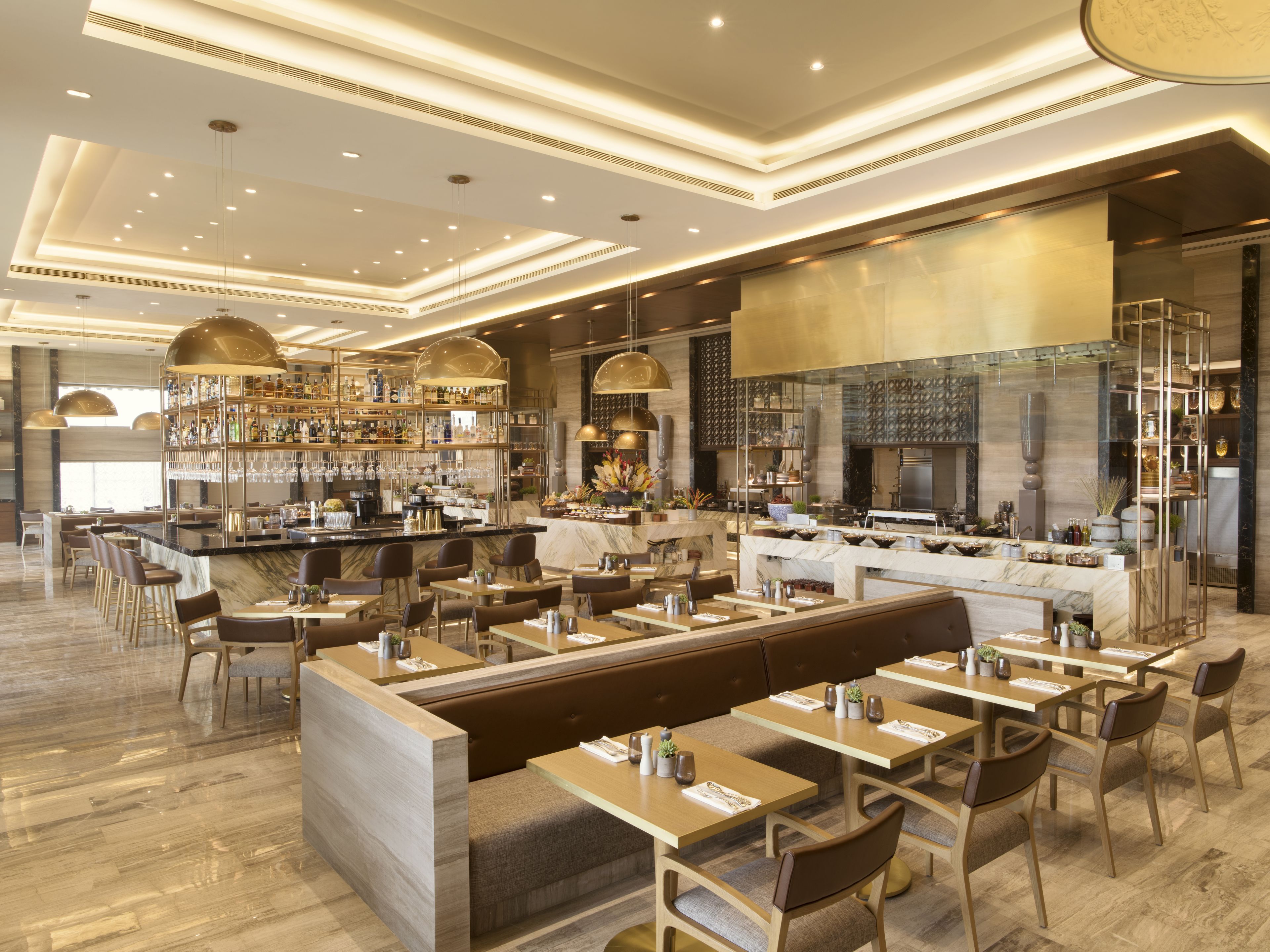 Ein modernes Restaurant mit Barbereich, Sitzgelegenheiten und einer durch eine Glasscheibe einsehbaren Küche.