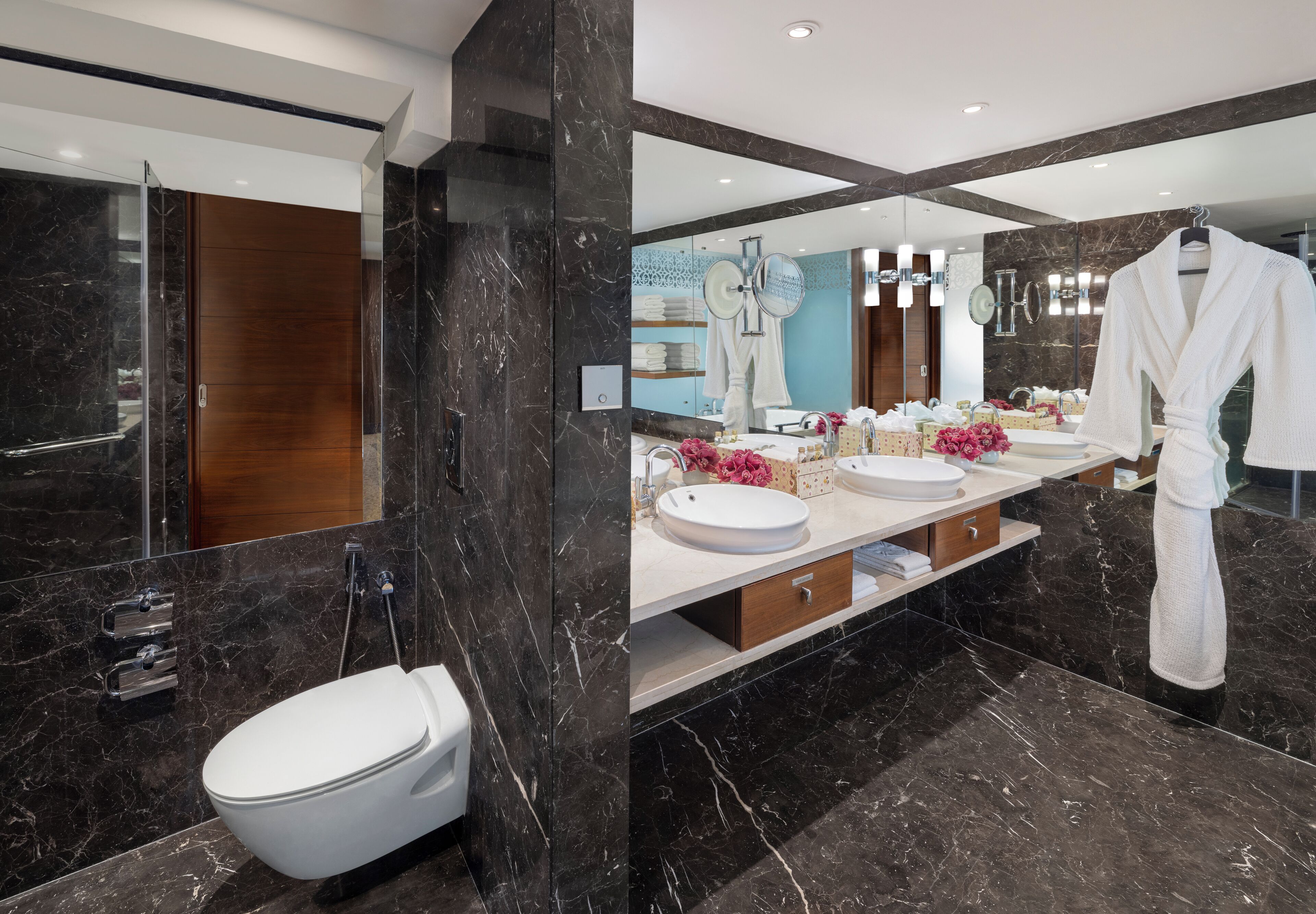 Een moderne badkamer met een grote spiegel, twee wastafels, een toilet en een badjas aan een rek.