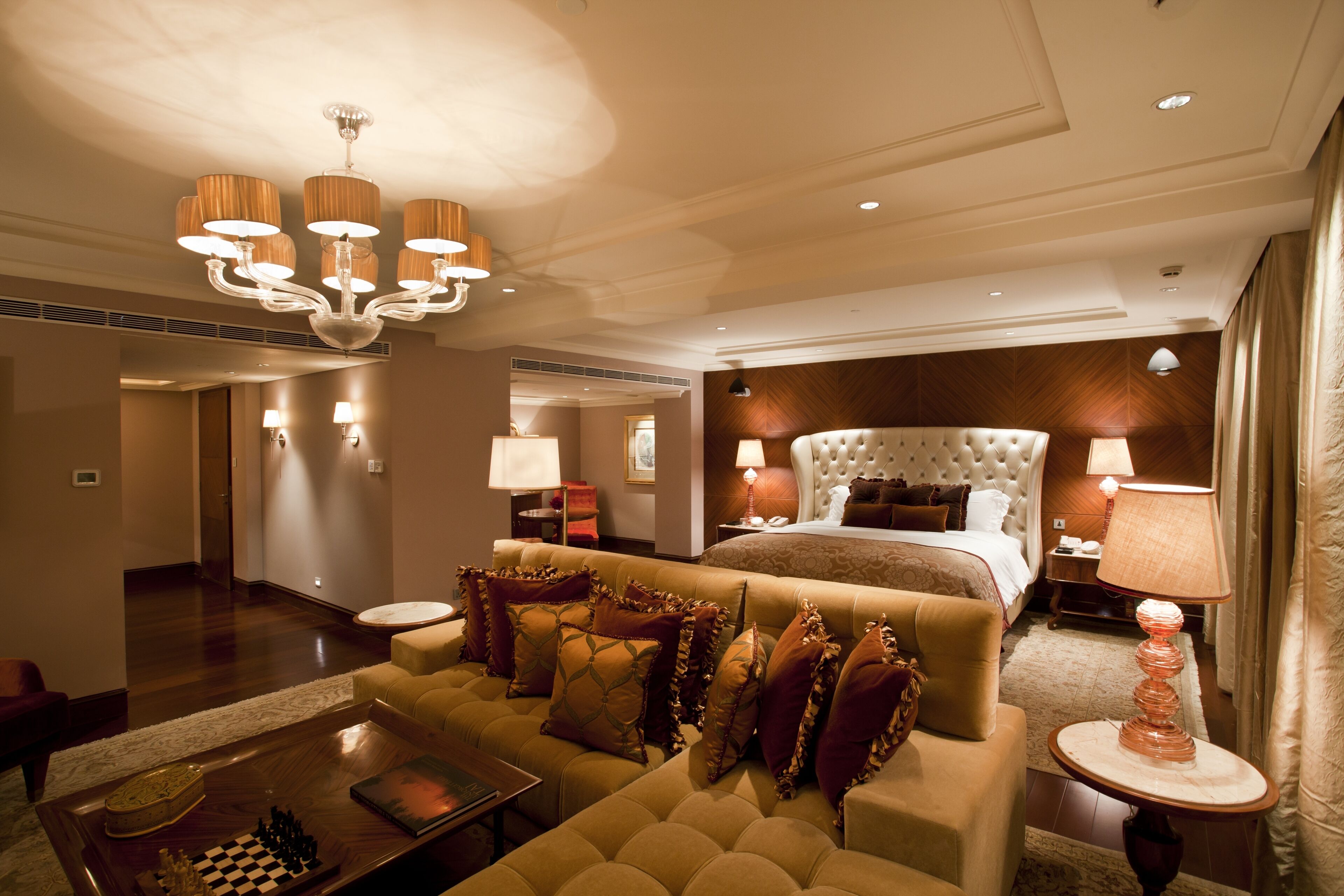A hotel room with a large bed, a sofa, a chandelier, and a chessboard on a side table.