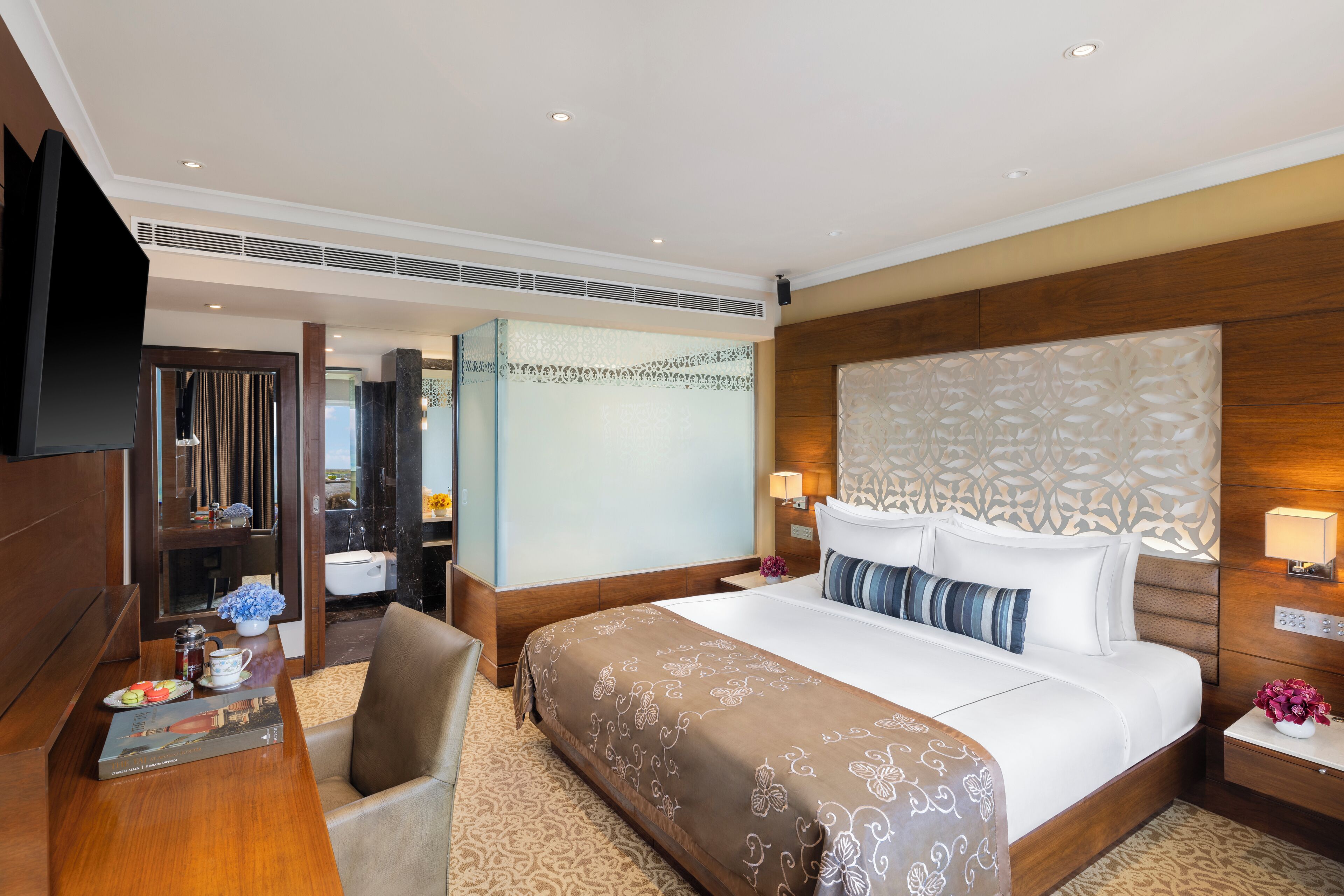 A hotel room with a large bed, a desk with a coffee maker, a chair, and a TV.
