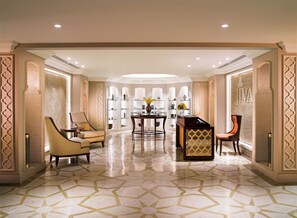 A spacious lobby with a geometric patterned floor, a central table with chairs, and decorative shelving with vases.