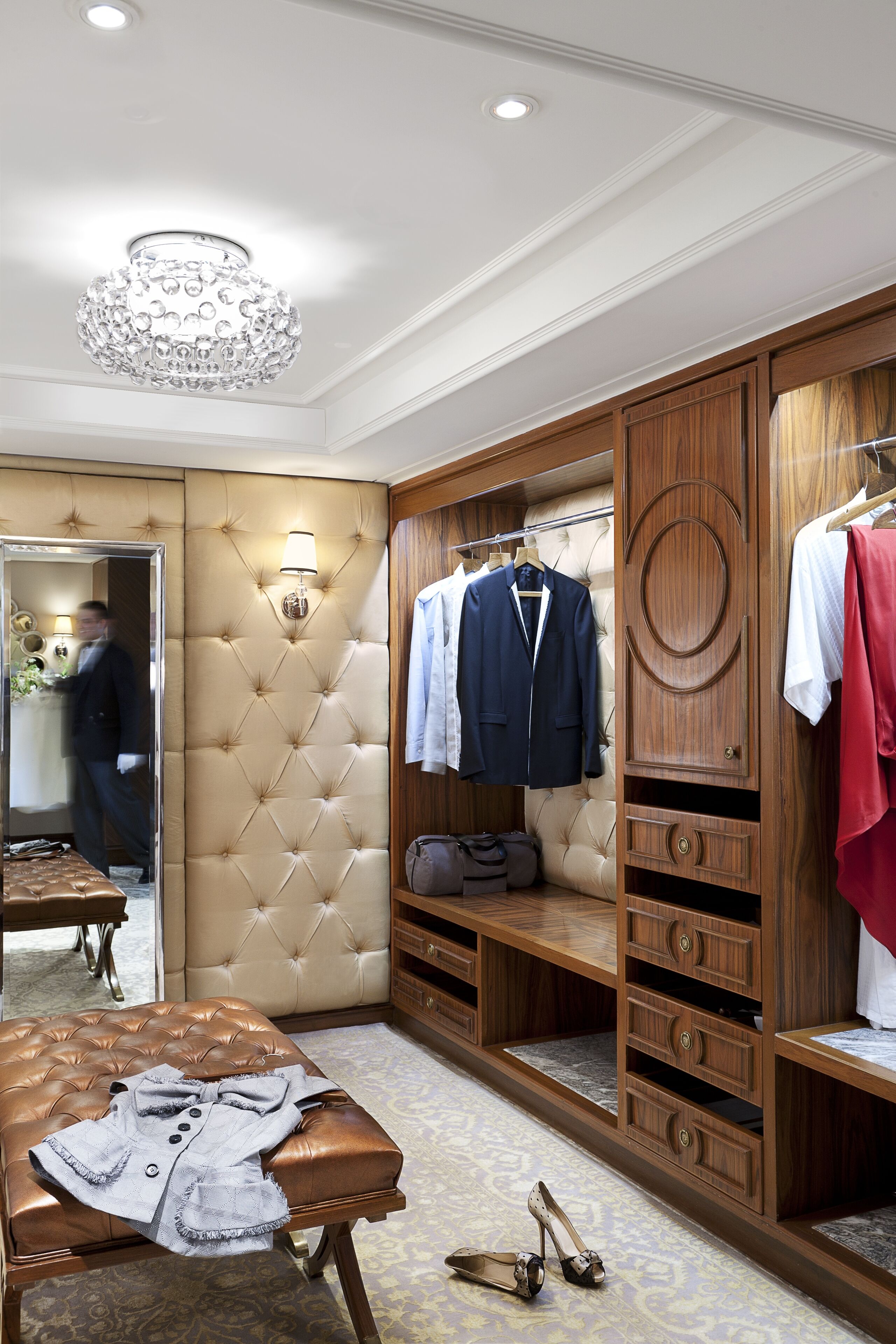 A well-appointed walk-in closet with a mirrored wardrobe, a tufted headboard, and a large chandelier.