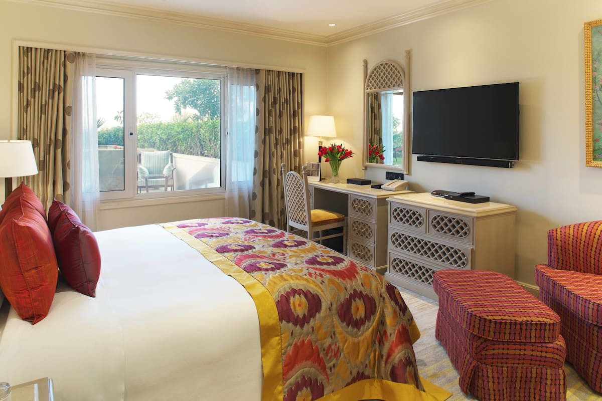 A hotel room with a large bed, a desk with a lamp, a television, and a view of the outdoors.