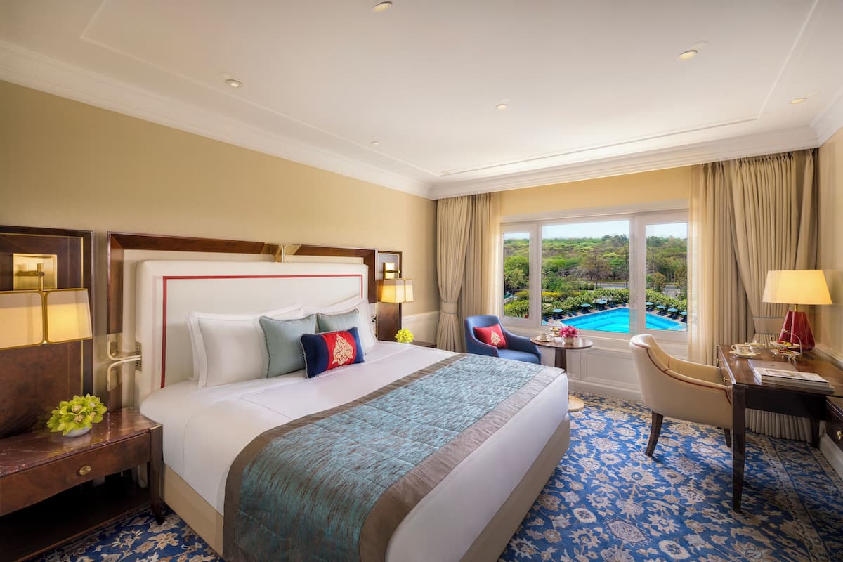 A hotel room with a large bed, a desk, a chair, a view of a pool, and a window with curtains.